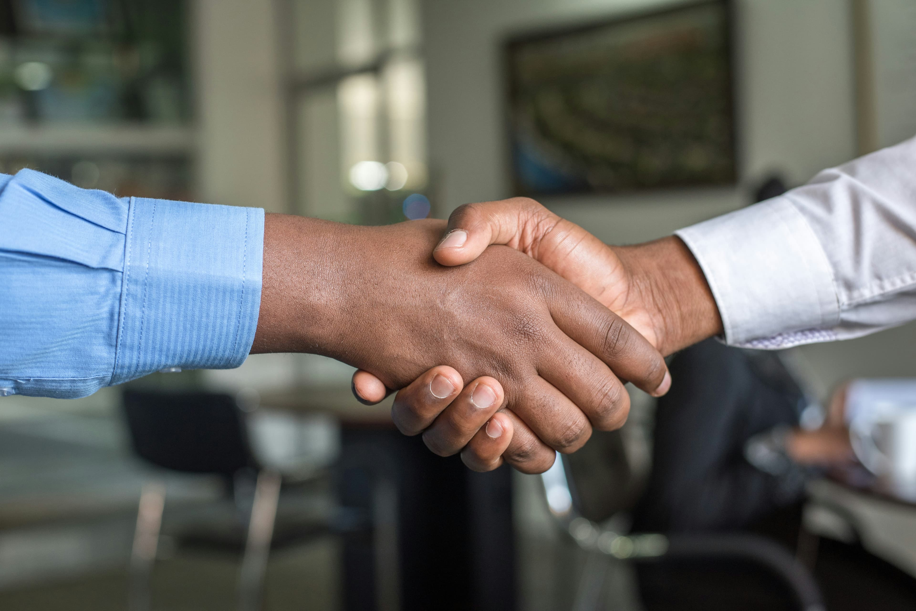 Partners Two people giving a handshake in a formal, office setting that is blurred in the background.